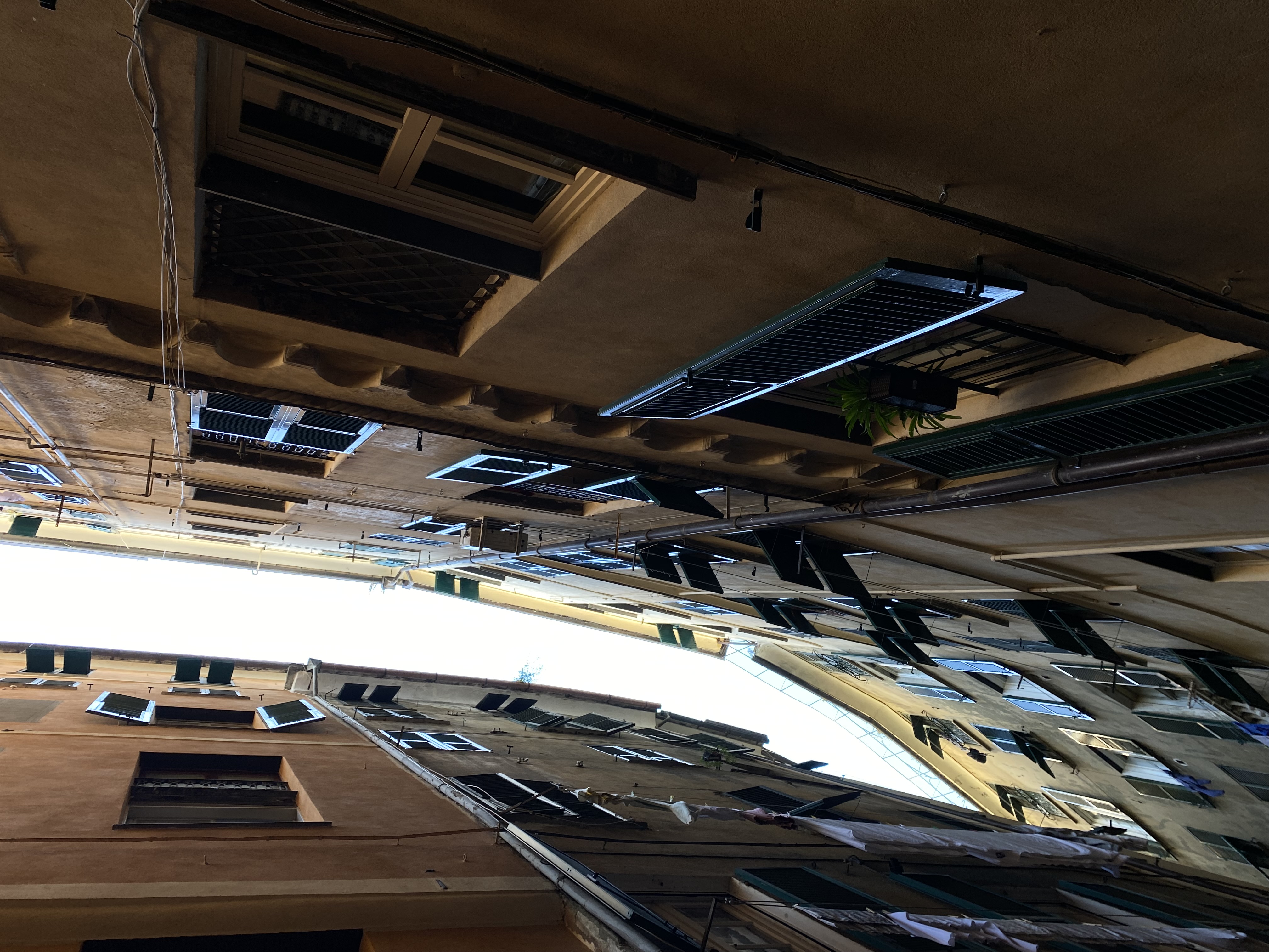 Looking straight up through a Genova caruggio, ancient shuttered windows closing in overhead, strip of sky above