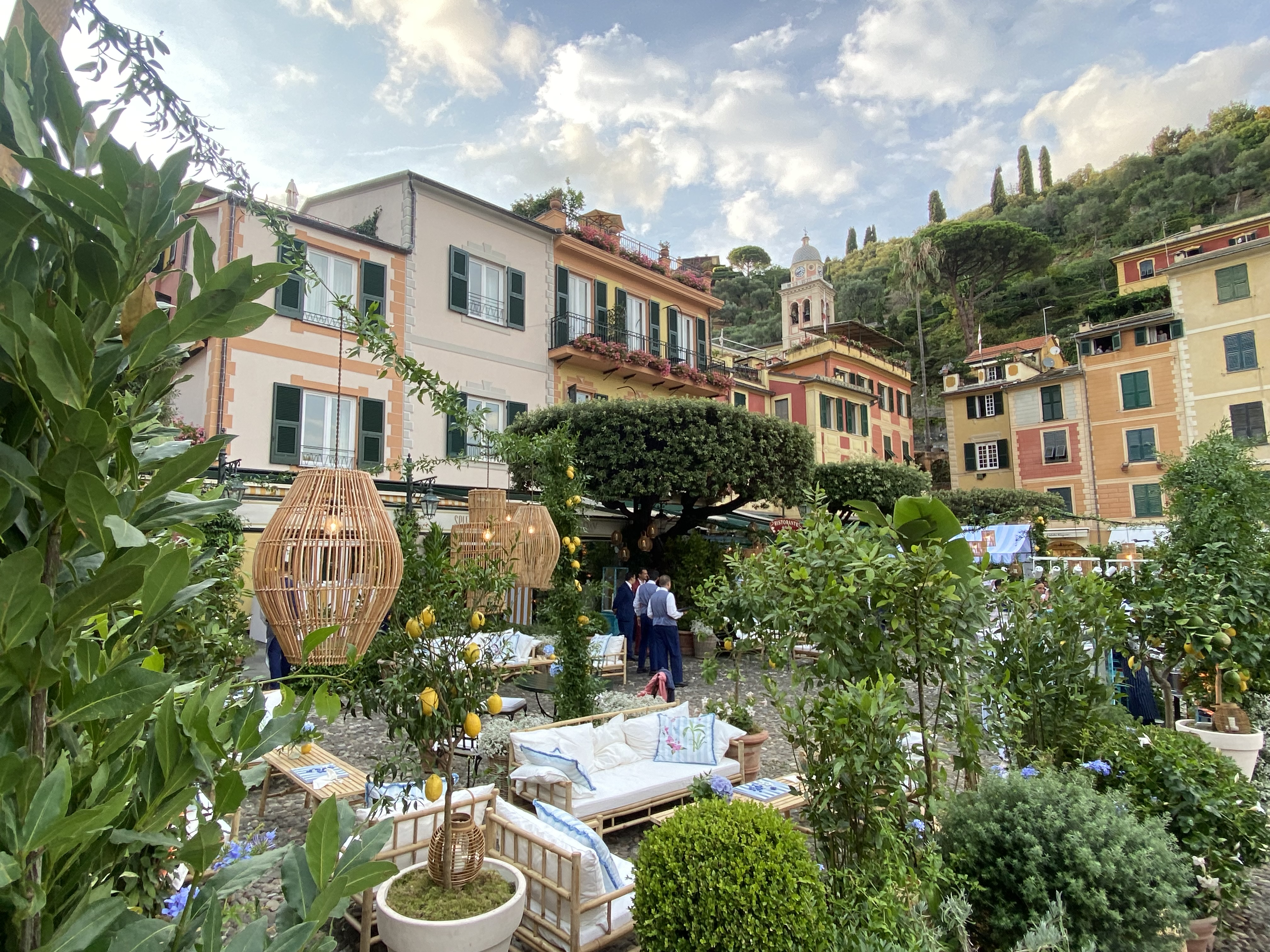 Portofino piazza garden terrace with lemon trees, wicker lanterns, and pastel Ligurian buildings beyond
