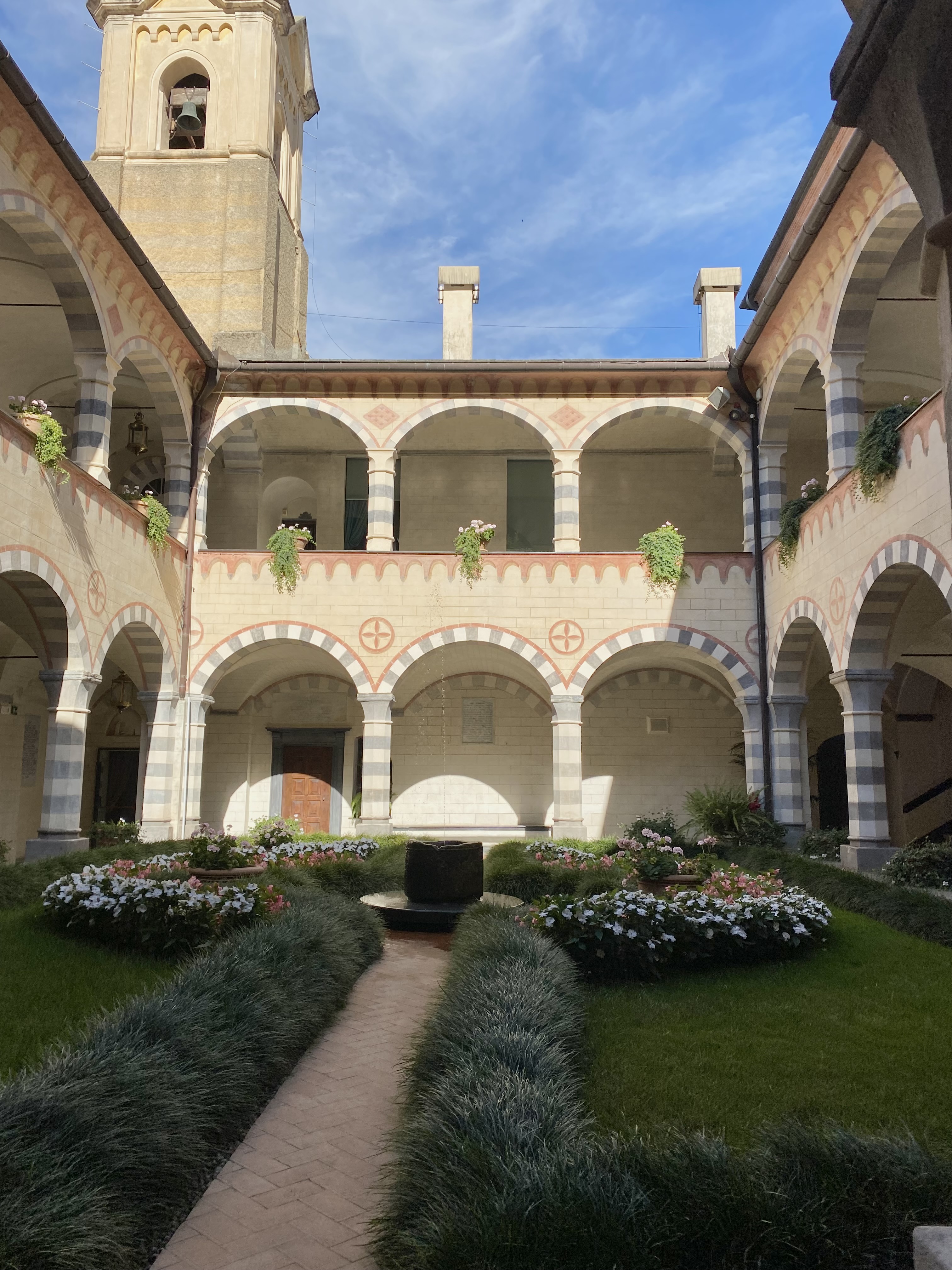 Genova monastery cloister with striped stone arches, flower garden and bell tower beyond